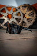 Black sunglasses with reflective lenses on a textured surface with gears in the background