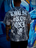 Man wearing a camo t-shirt with text saying, "trust no one" against a graffiti-covered wall